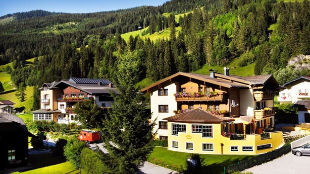 A multi-story chalet with a sloped roof, balconies with flower boxes, and a view of a forested mountain. - Pension Anja (Kleinarl)
