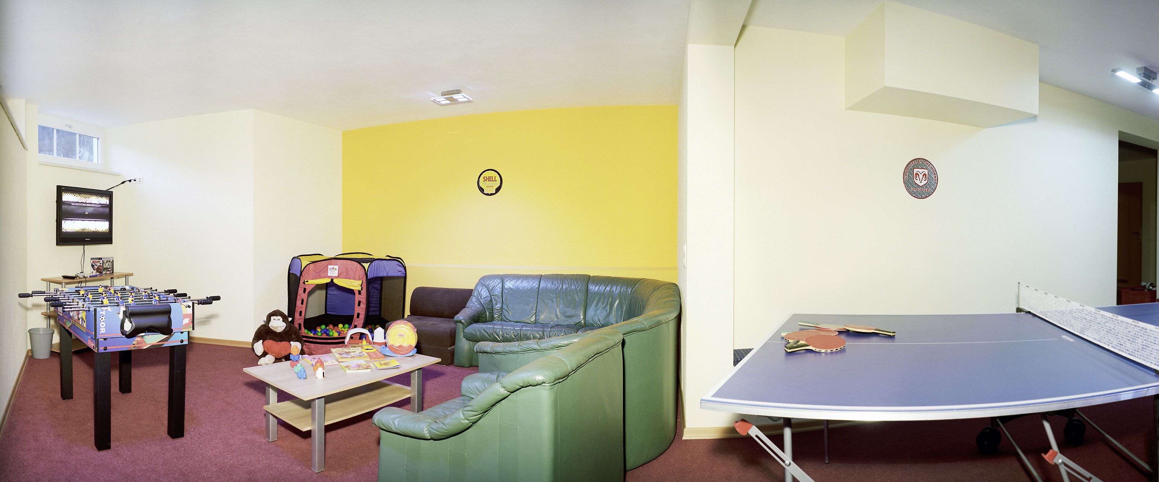 A room with a foosball table, a trampoline, a green couch, and a ping pong table.