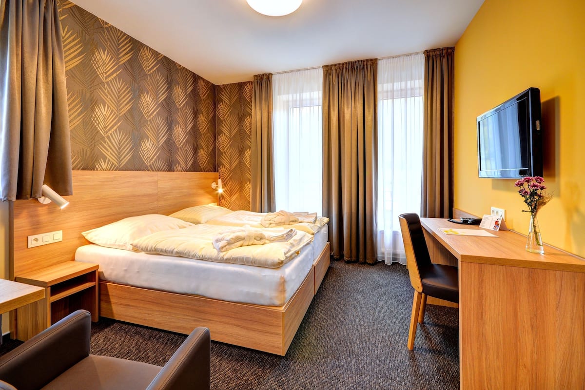 Ein Hotelzimmer mit Bett, Schreibtisch, Stuhl, Fernseher und Vorhängen.
