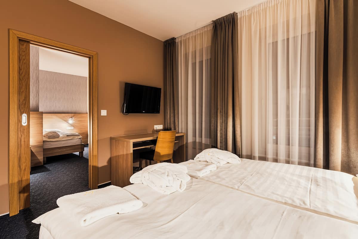 Ein Hotelzimmer mit Bett, Schreibtisch, Stuhl, Fernseher und einer Tür zu einem weiteren Raum.