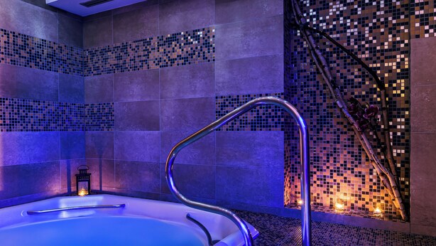 Un área de spa con hidromasaje, paredes alicatadas y un mosaico decorativo.