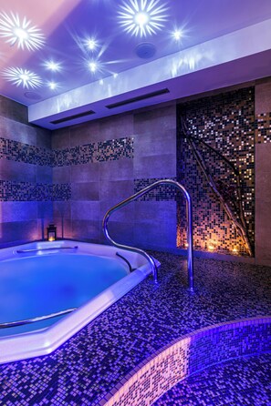 A spa area with a hot tub, tiled walls, and a decorative mosaic wall. - Hotel Helios (Lipova-Lazne)
