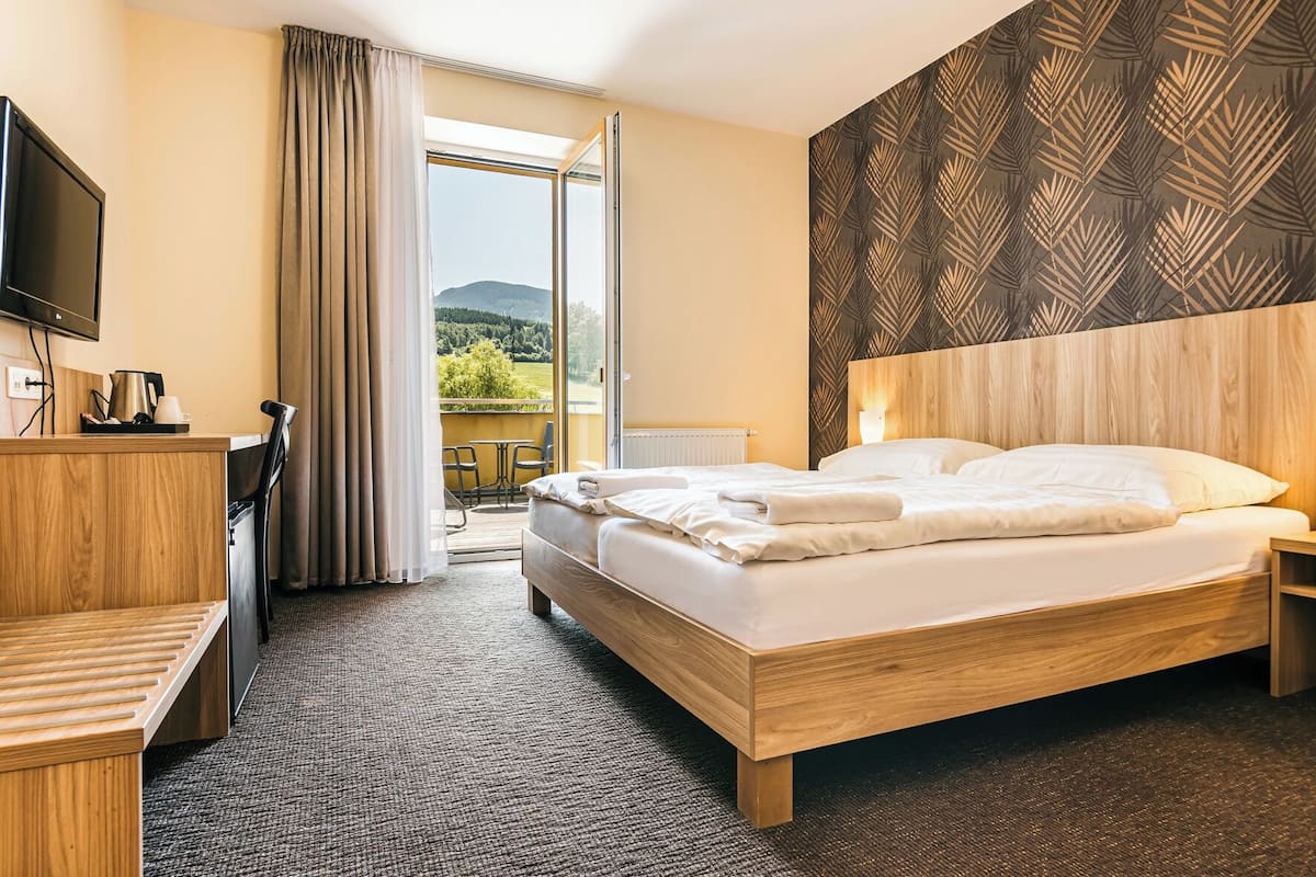 Ein Hotelzimmer mit Bett, Fernseher, Schreibtisch, Stuhl und einem Balkon mit Blick auf die Landschaft, sowie einer Wand mit Musterung.