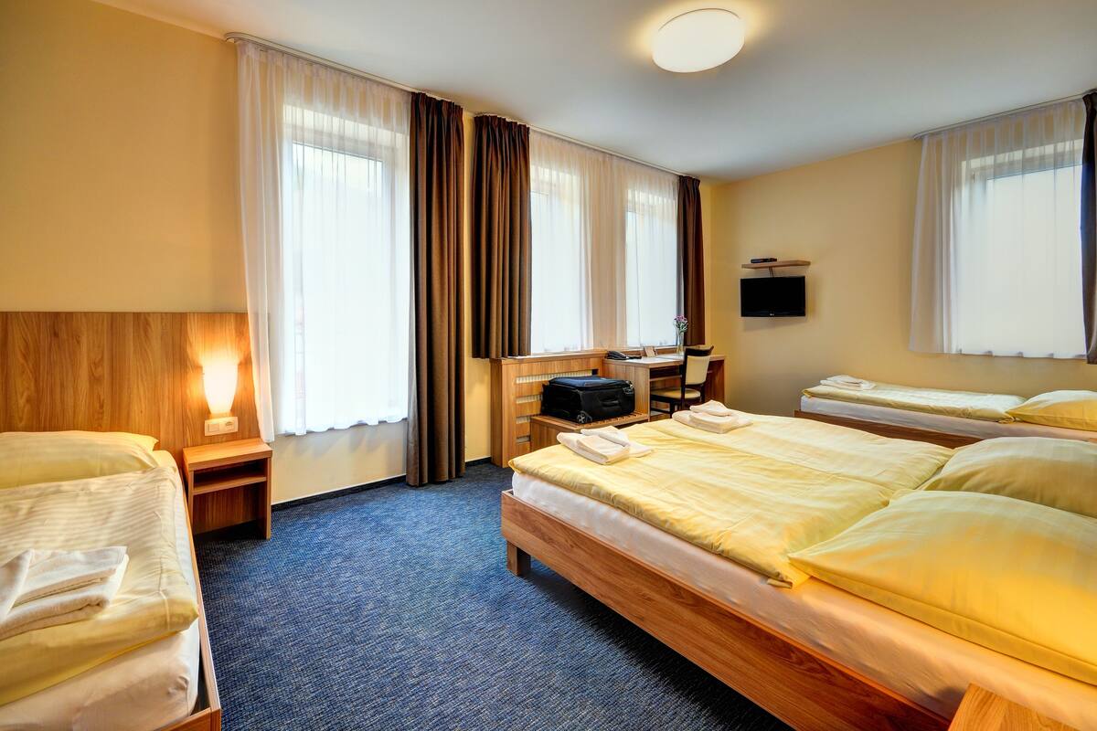 Ein Hotelzimmer mit zwei Betten, einem Schreibtisch, einem Stuhl, einem Fernseher und einem Fenster mit Vorhängen.