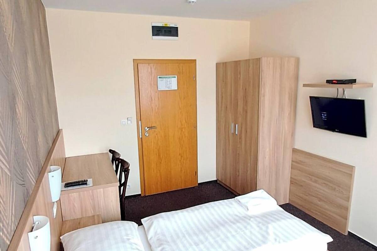 Ein Hotelzimmer mit Bett, Schreibtisch, Stuhl, Kleiderschrank, Fernseher und einer Tür.