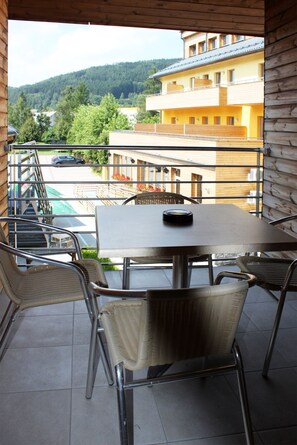 A balcony with a table and chairs, overlooking a swimming pool and a building with a yellow facade.