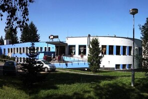 Un edificio con fachada curva, una entrada pequeña y un estacionamiento con coches.