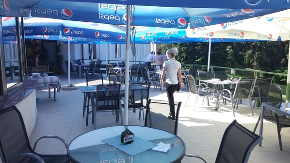 Un área de patio al aire libre con mesas y sillas, cubierta por sombrillas con la marca Pepsi.