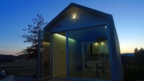 A modern, glass-walled building with an open entrance and a dining area visible inside.