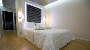 A bedroom with a bed, a headboard, two wall sconces, and a wooden floor.