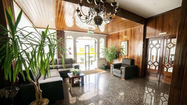 A lobby with a polished floor, wooden paneling, a chandelier, and potted plants.