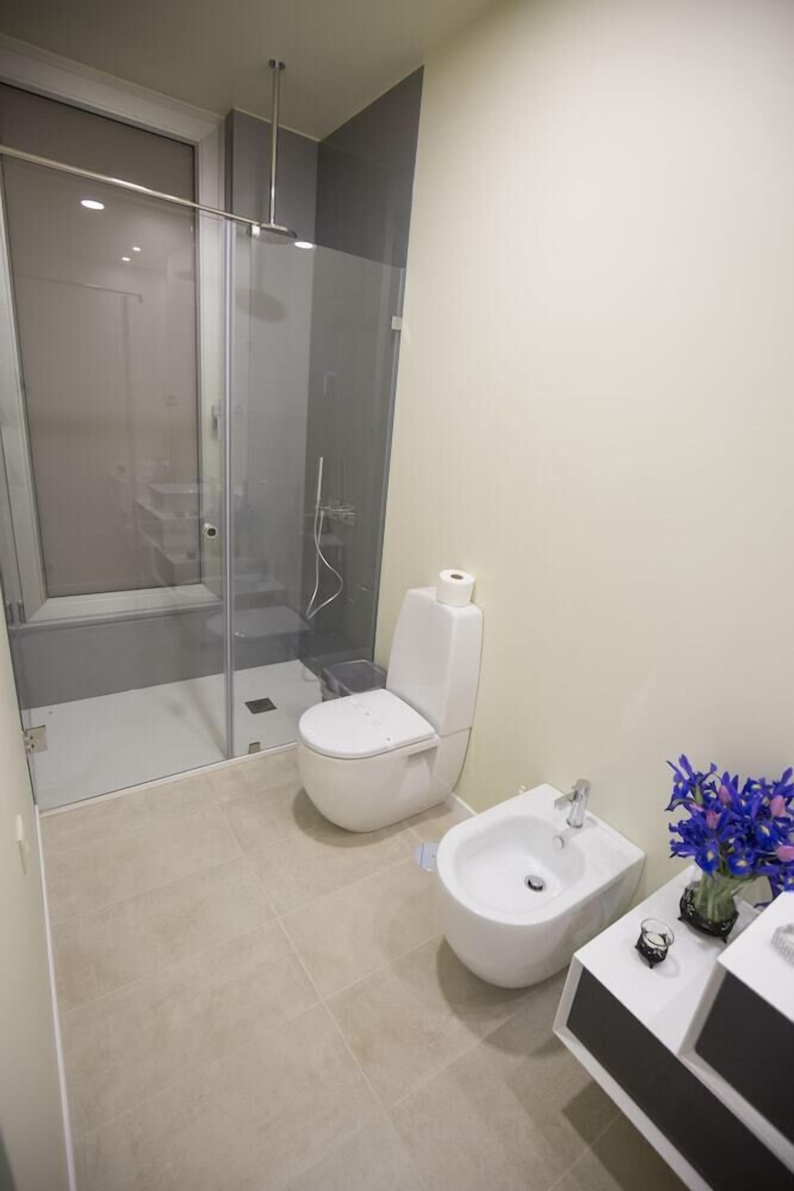 A modern bathroom with a glass-enclosed shower, a toilet, a bidet, and a sink with a mirror.