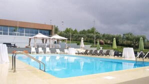 A swimming pool with lounge chairs and umbrellas, a covered seating area, and a building in the background.