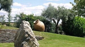 A stone structure and a large pot in a grassy outdoor area with trees and a stone wall in the background.