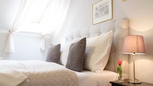 A neatly made bed with a quilted cover, a bedside lamp, and a vase with a flower on a nightstand. - U Solné Brány (Ceské Budejovice (Budweis))