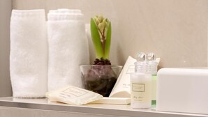 Un baño con toallas blancas, un florero de vidrio con una planta y artículos de aseo en un estante.