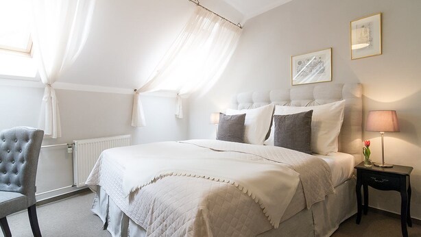 Un dormitorio con una cama grande, una mesita de noche con lámpara, una silla y cortinas de encaje.