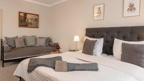 Un dormitorio con una cama grande, un sofá, una mesita de noche y dos cuadros en la pared.