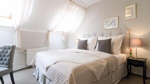 A bedroom with a bed, a chair, a bedside table with a lamp, and a window with curtains. - U Solné Brány (Ceské Budejovice (Budweis))