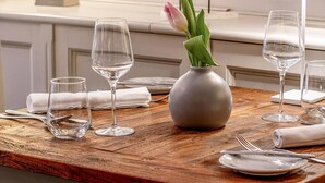 Una mesa de comedor dispuesta con copas de vino, un florero con una flor y una escultura de pájaro.