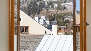 A room with a large window overlooking a mountainous landscape with a castle-like structure. - Hotel Binggl (Mauterndorf)