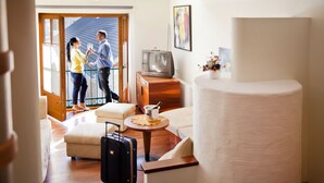 A hotel room with a wooden floor, a sofa, a small round table with a lamp, a television on a wooden stand, and a large cylindrical object, possibly a decorative piece. - Hotel Binggl (Mauterndorf)