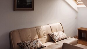 A cozy living room with a beige sofa, two patterned cushions, a wooden coffee table, and a framed picture on the wall. - Amphone (Brno)