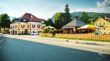 Straßenansicht mit einem Hotel, einem Café und einer Bergkulisse.