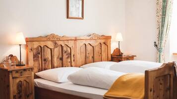 Ein hölzernes Bett mit zwei Kissen und einer Decke, neben dem Nachttische mit Lampen und ein gerahmtes Bild über dem Bett stehen.