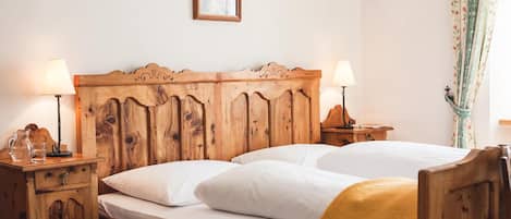 A wooden bed with two pillows and a blanket, flanked by nightstands with lamps and a framed picture above.