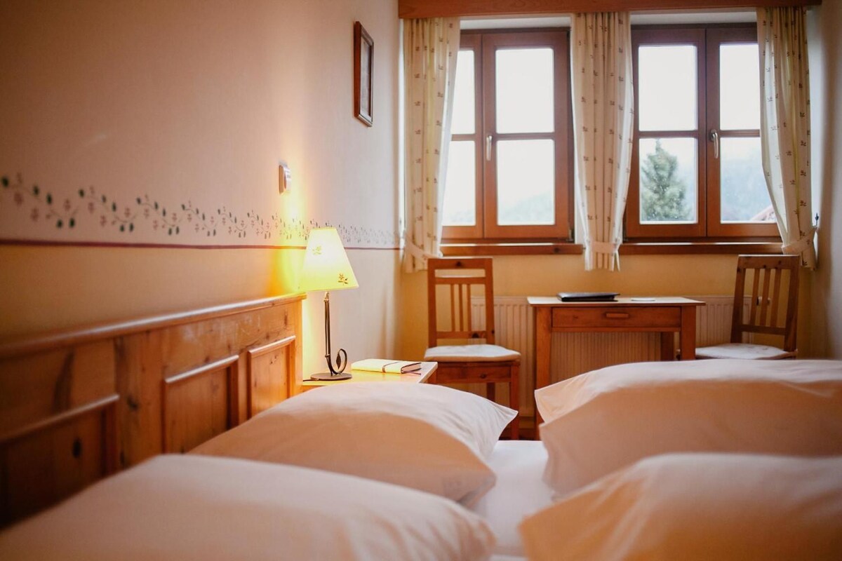 Une chambre d’hôtel avec deux lits, un bureau, une chaise, une lampe et une fenêtre avec des rideaux.