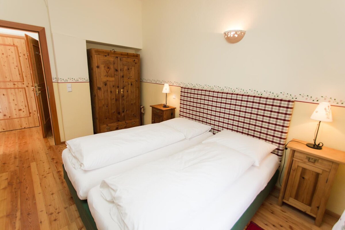 Un lit double avec du linge de lit blanc, une armoire en bois, une petite table de chevet avec une lampe et une tête de lit à carreaux.