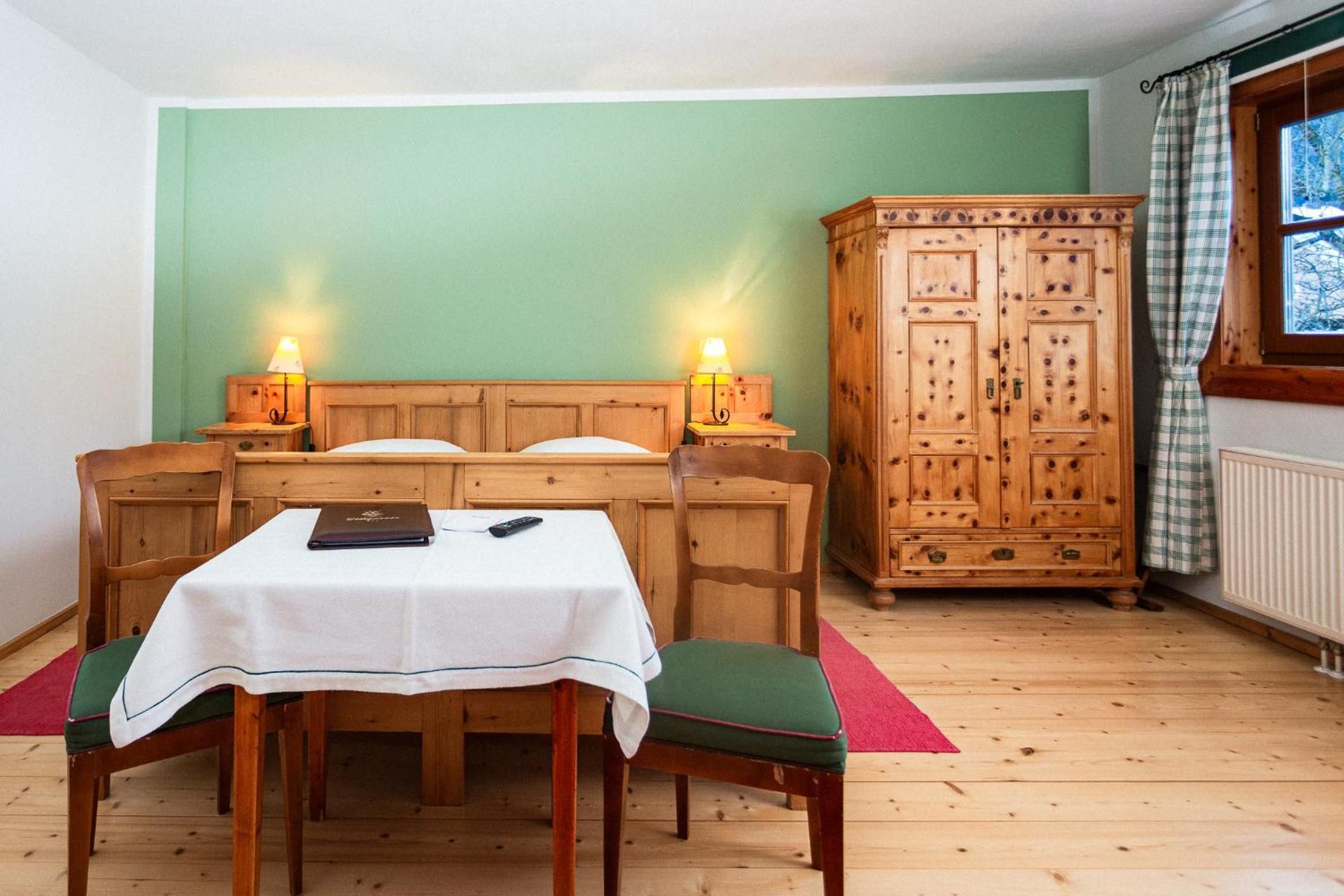 Ein Zimmer mit einem hölzernen Bett, einem Tisch mit weißer Tischdecke, zwei Nachttischlampen, einem Holzschrank und einem Fenster mit Vorhängen.
