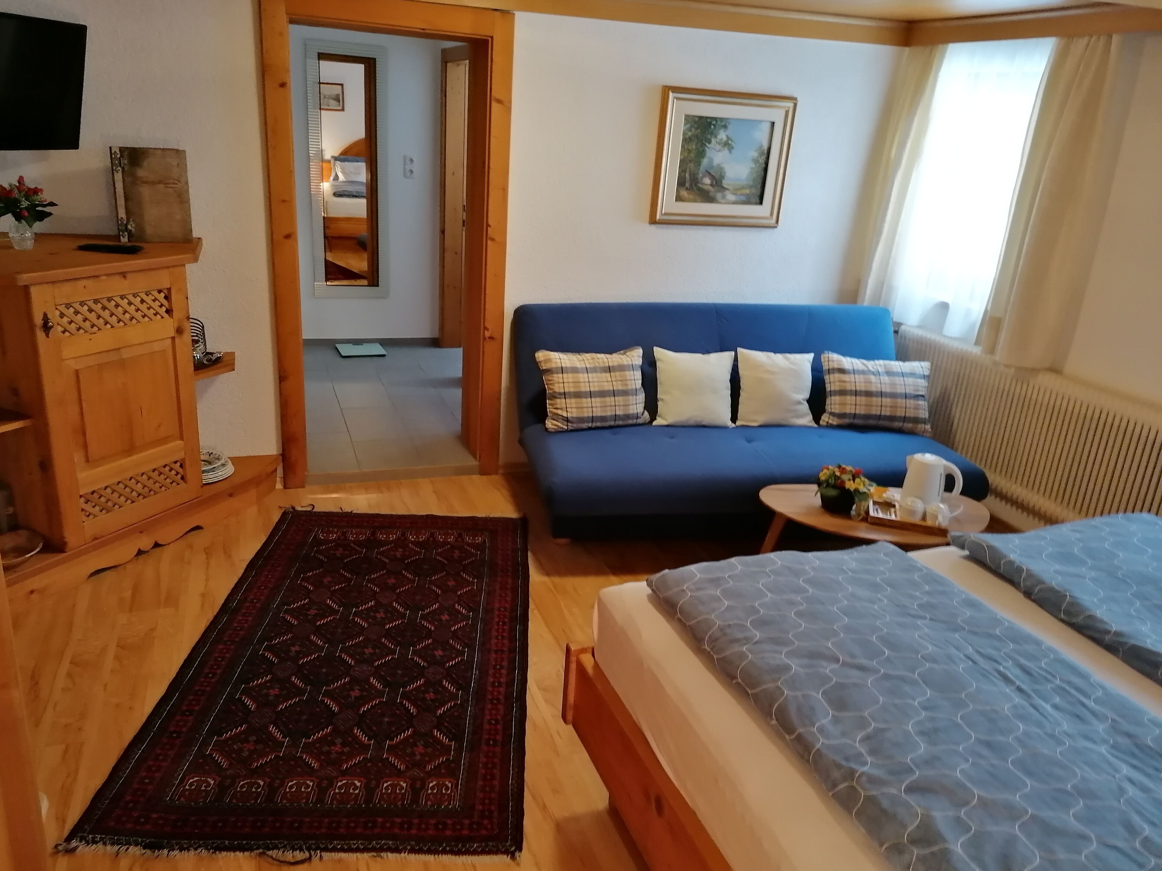 A cozy room with a blue sofa, a wooden cabinet, a bed with a patterned bedspread, and a small table with a tray.