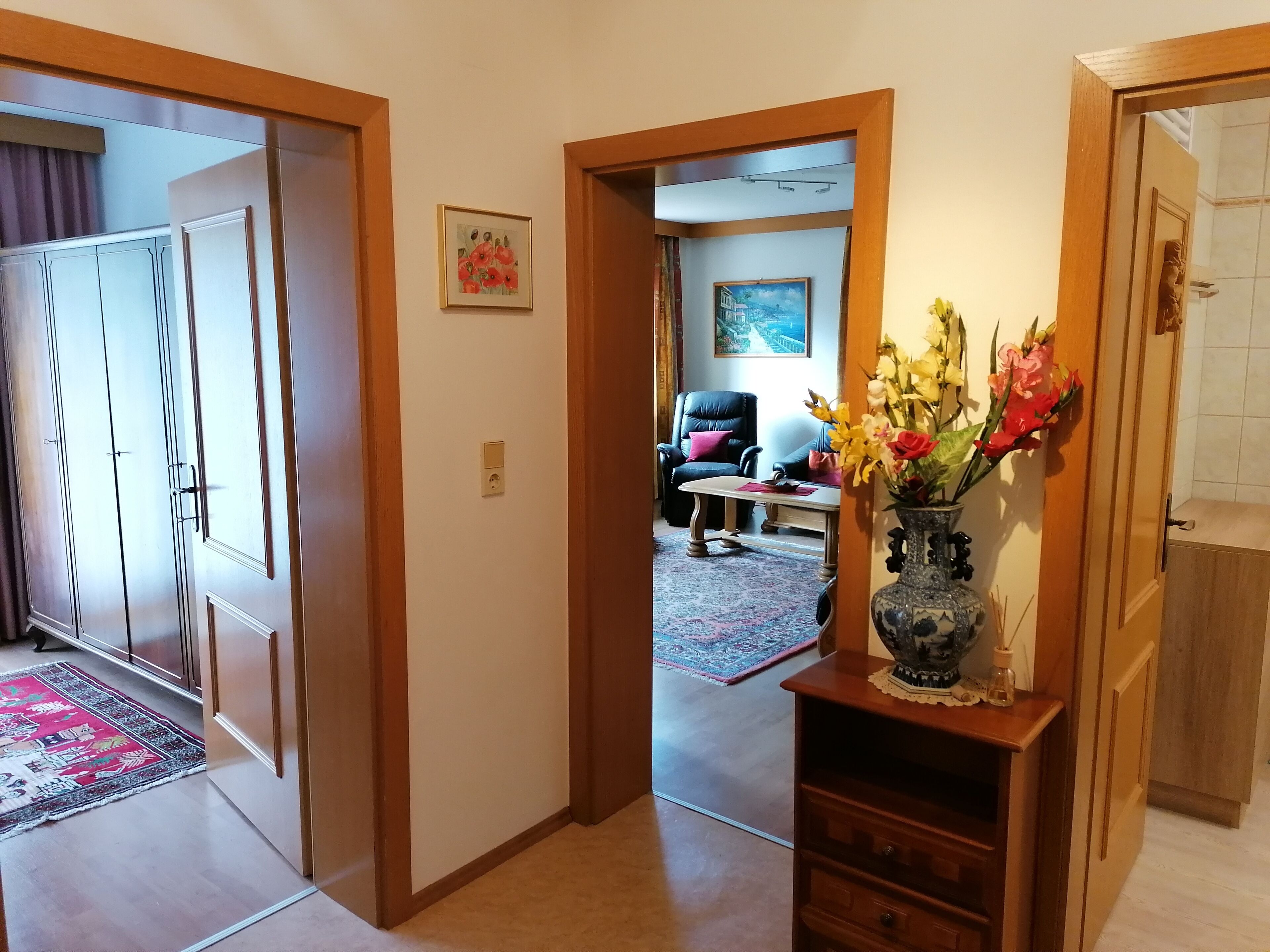 Ein Flur mit einer Holztür, einem Blumenstrauß in einer Vase und einem Gemälde an der Wand.