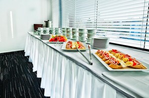 Mesa de buffet com diversos alimentos e pratos empilhados.