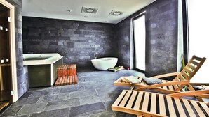 Un baño moderno con piso de piedra, una bañera independiente, una silla de madera y un banco de madera.