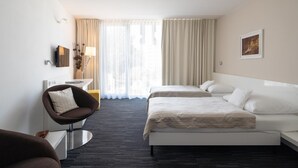 Habitación de hotel con cama, una silla, escritorio y ventana con cortinas.
