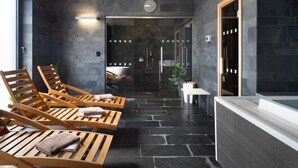 Un moderno espacio de spa con tumbonas de madera, ducha con cerramiento de vidrio y suelo de baldosas de piedra.