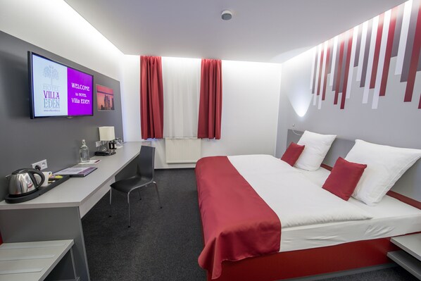 Una habitación de hotel con cama, escritorio, silla y televisor mostrando el nombre del hotel.