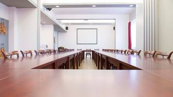 A conference room with a long table and chairs, white walls, and a large window.