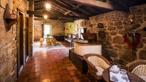 Ein rustikales Interieur mit Steinwänden, Holzbalken, Korbmöbeln und einem Kamin aus Stein.