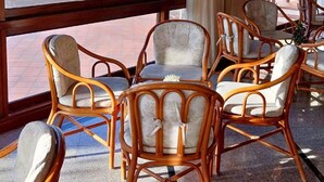 Ein Zimmer mit Korbstühlen und einem Tisch, große Fenster mit Blick auf den Strand und ein Gebäude.