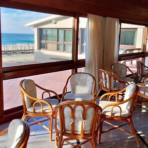 A room with wicker chairs and a table, large windows with a view of the beach and a building. - Estalagem de Santo Andre (POVOA DE VARZIM)