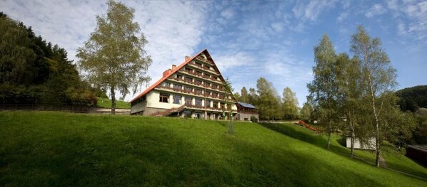 A multi-story building with a sloped roof, surrounded by lush green grass and trees.