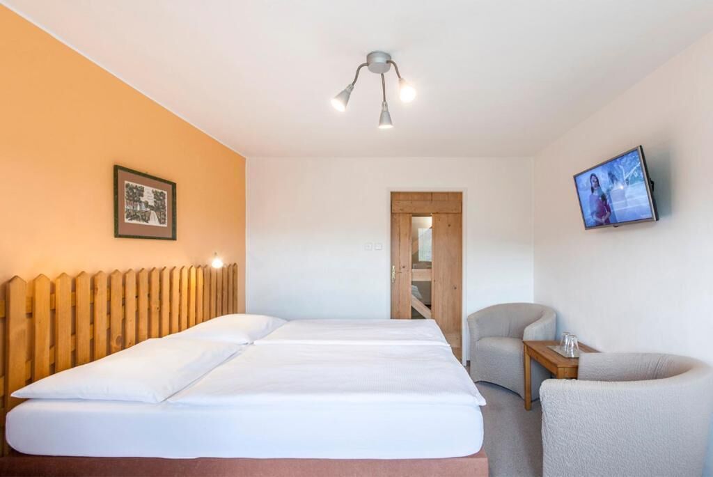 A hotel room with a bed, a wooden headboard, a TV mounted on the wall, and a small table with a chair.