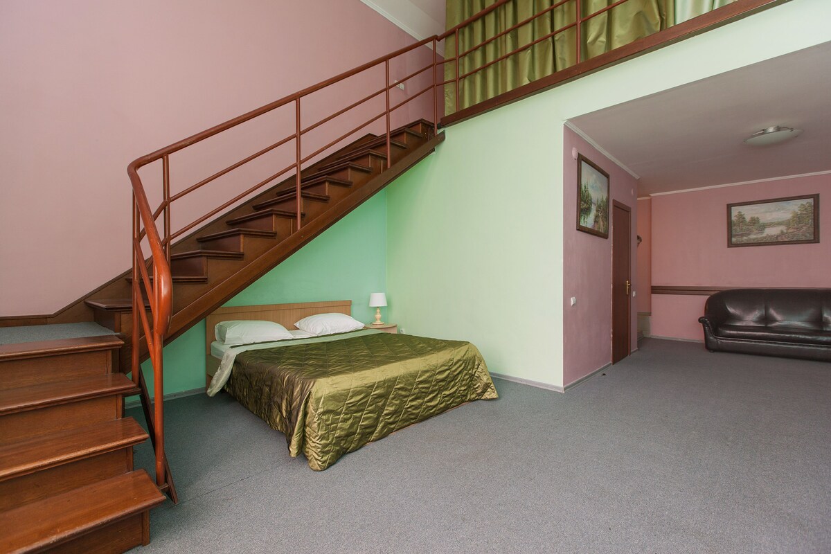 Un dormitorio con una cama, una escalera de madera, un sofá y una puerta que da a otra habitación.