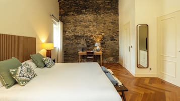 Un dormitorio con una cama grande, cabecera de madera, pared de piedra, una mesita con lámpara y un espejo en la pared.