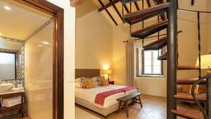 Un dormitorio con cama, mesitas de noche, un banco, una escalera de madera y un baño con lavabo y toallas.
