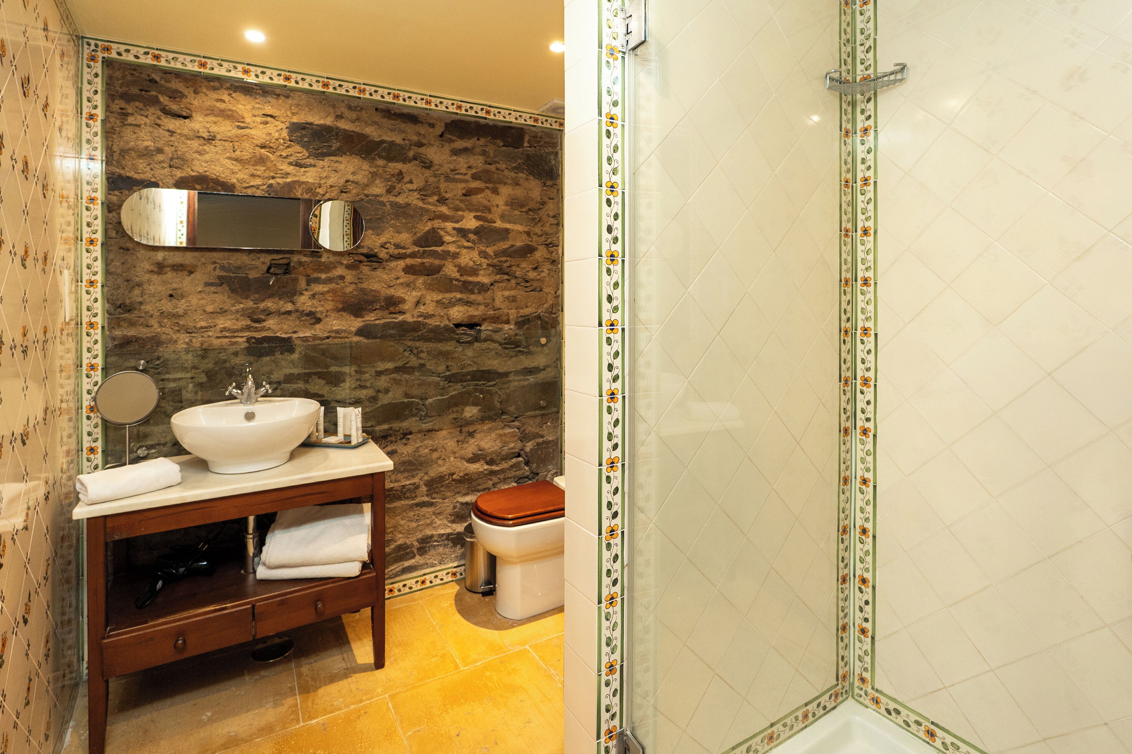 Un baño con pared de piedra, tocador de madera con lavabo e inodoro.